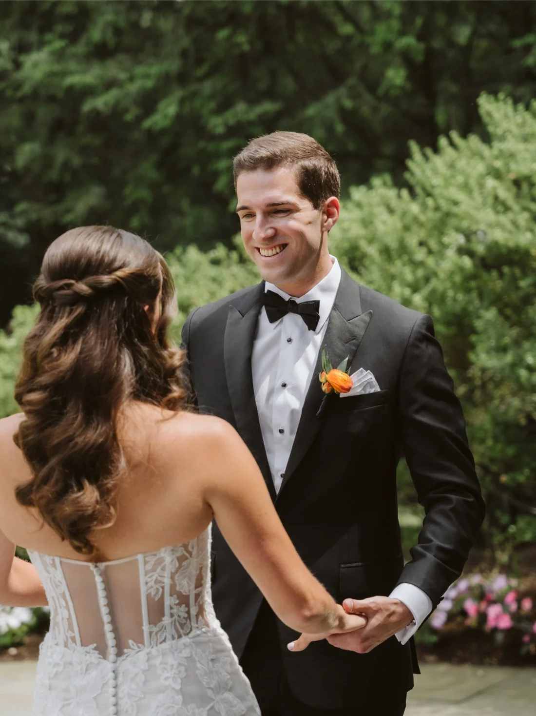 Sydney and Matt hold hands and smile during their Tappan Hill Mansion wedding first look, surrounded by lush garden greenery.
