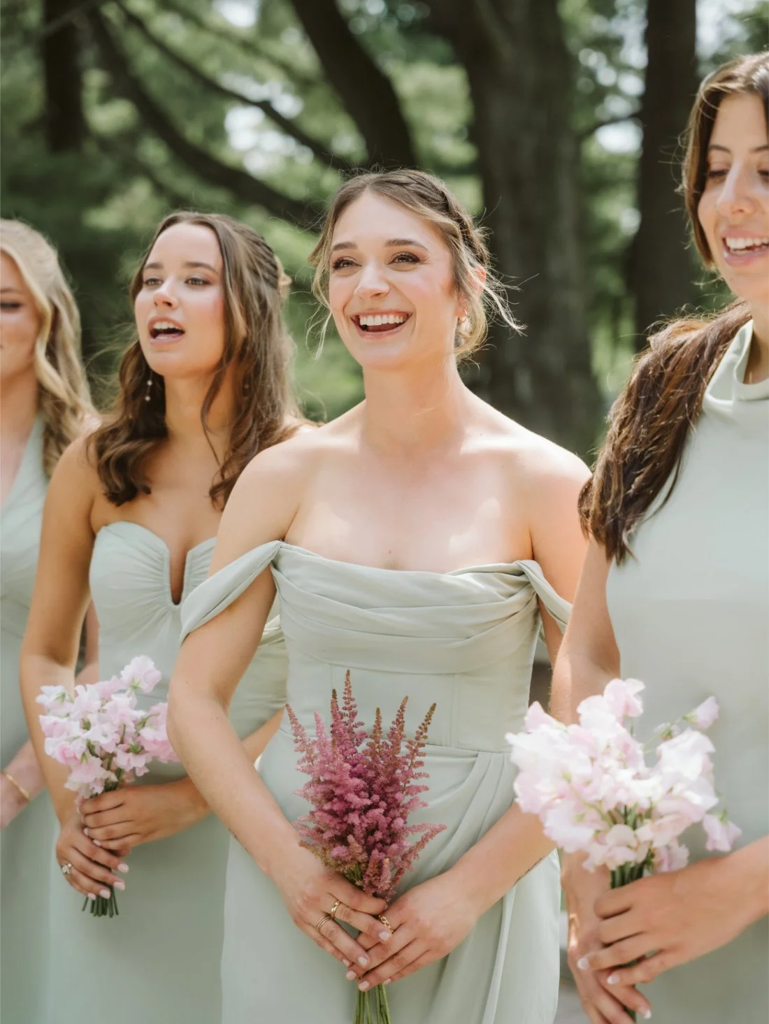 Bridesmaids in sage green dresses hold pink floral bouquets and share a laugh during Sydney and Matt’s Tappan Hill Mansion wedding.