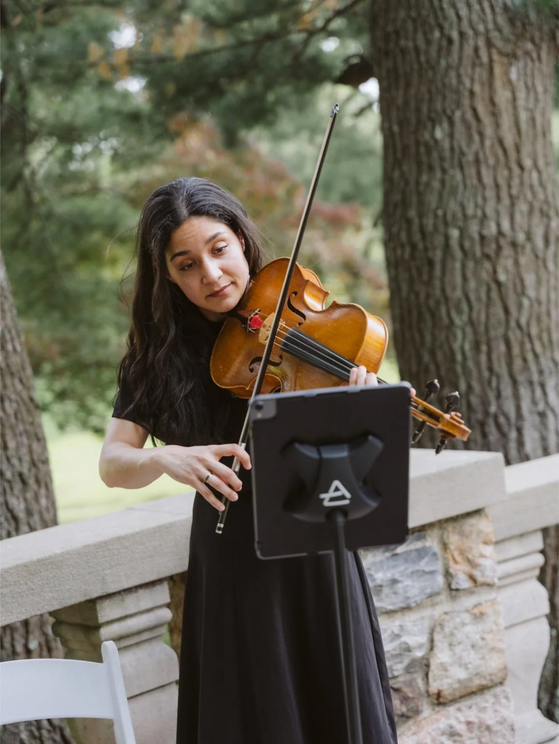 Violinist performing outdoors during a Tappan Hill Mansion wedding ceremony, surrounded by lush greenery and stone architecture.
