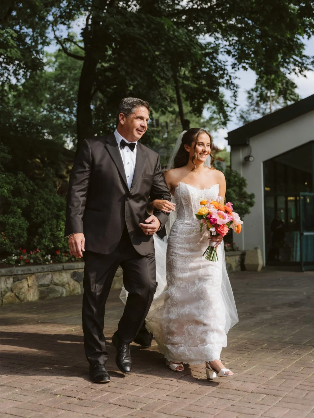 Sydney walks down the aisle with her father during their Tappan Hill Mansion wedding, carrying a vibrant pink and orange bridal bouquet.
