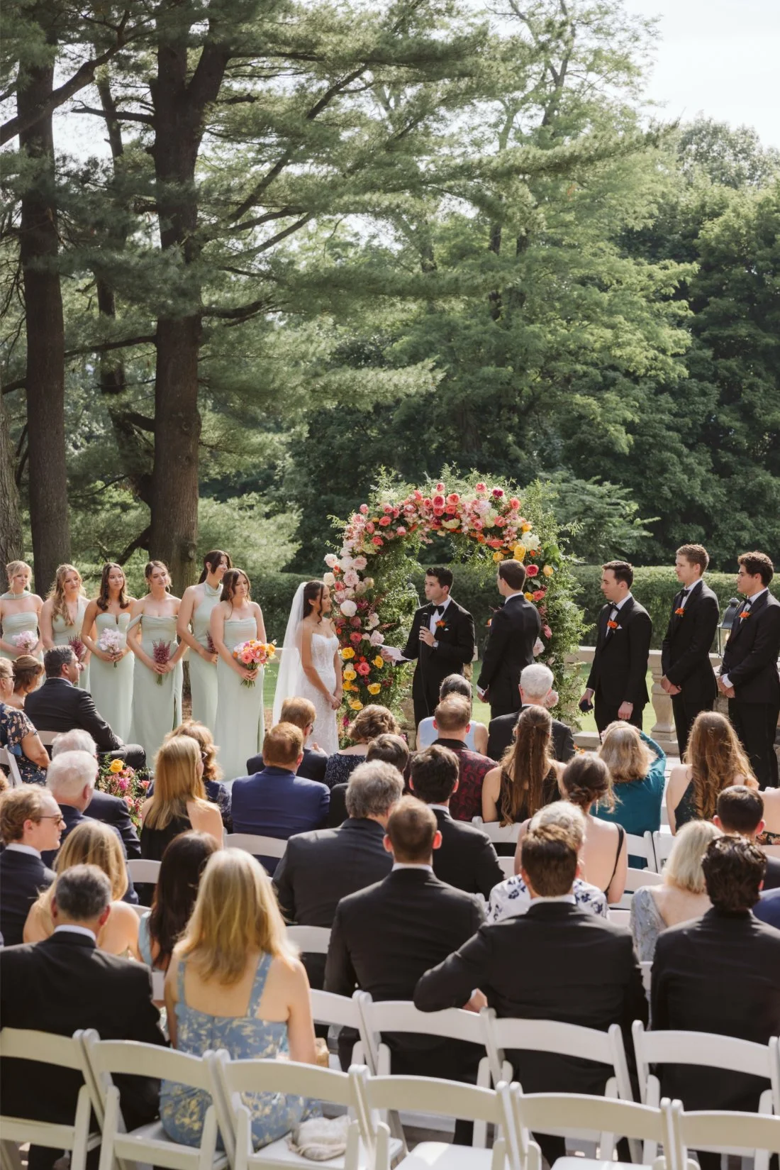 Sydney and Matt exchange vows beneath a colorful floral arch during their outdoor Tappan Hill Mansion wedding ceremony.