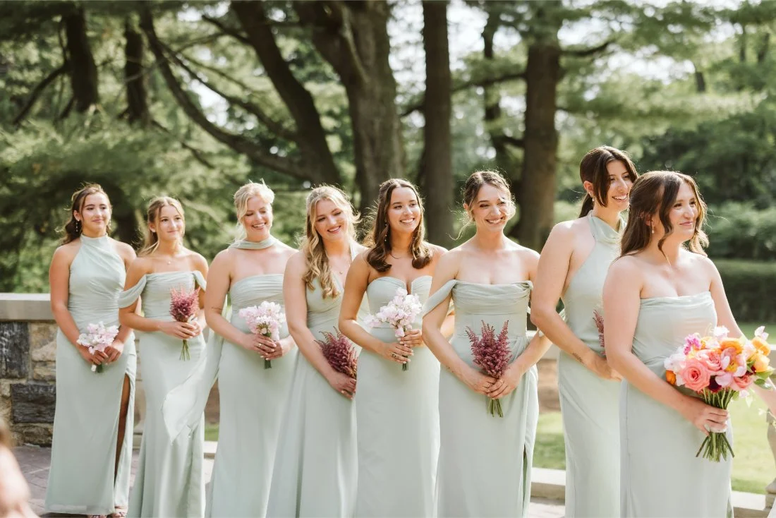 Bridesmaids in sage green dresses hold pink and coral bouquets while watching Sydney and Matt exchange wedding vows.