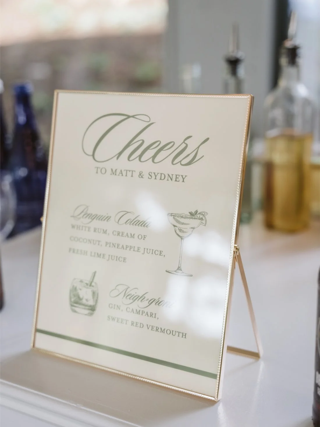 Custom wedding cocktail menu featuring Sydney and Matt's signature drinks, a Penguin Colada and Negroni, displayed in a gold frame.
