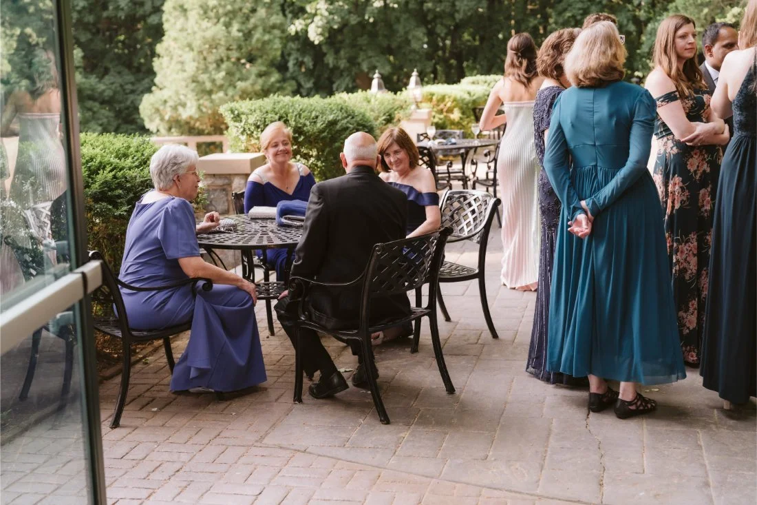 Wedding guests enjoying cocktail hour on the outdoor terrace at Tappan Hill Mansion, surrounded by lush greenery and scenic Hudson River views.