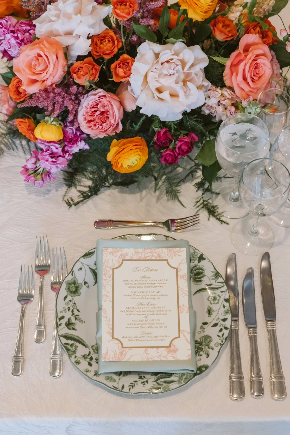 Tappan Hill Mansion wedding reception place setting featuring a custom dinner menu, green floral china, sage napkin, and vibrant pink and orange flowers.