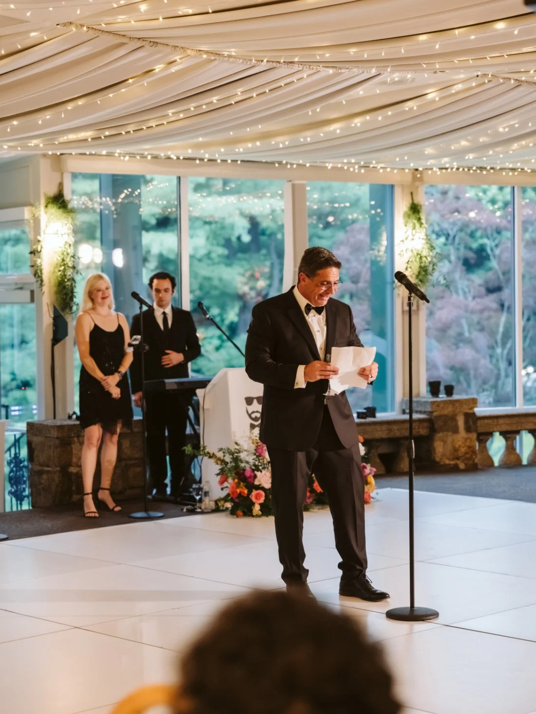 Wedding guest delivering a heartfelt speech beneath a draped ceiling with twinkling string lights at Tappan Hill Mansion.