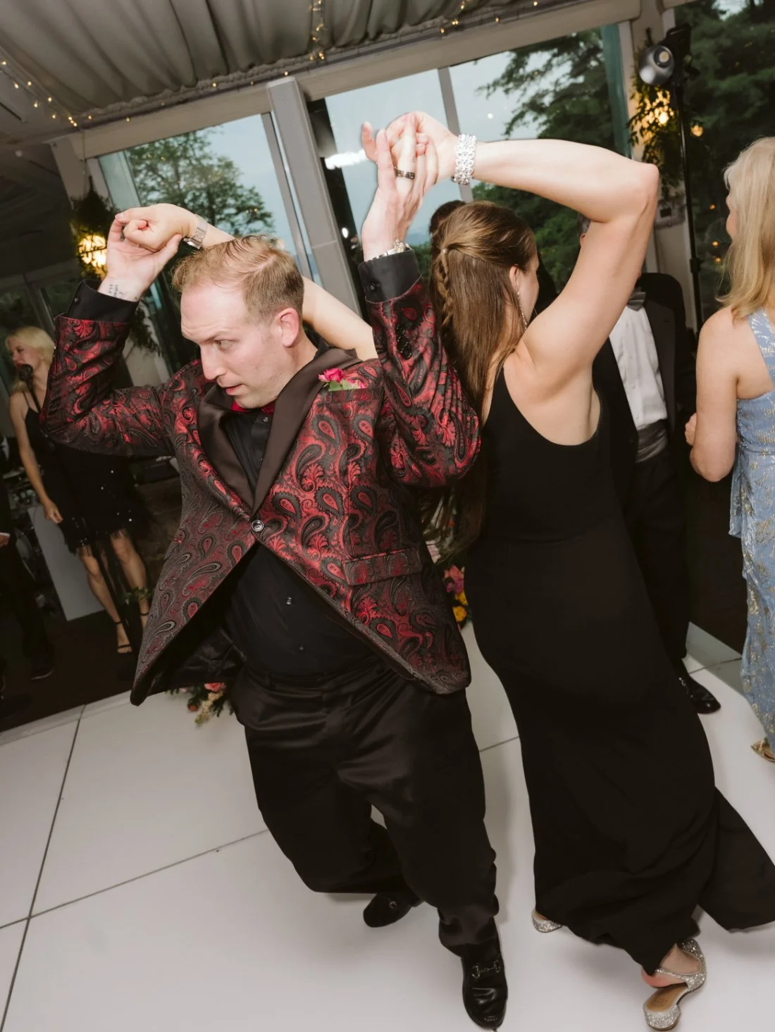 Wedding guest in a red and black patterned jacket dancing with a guest in a black dress at Tappan Hill Mansion.