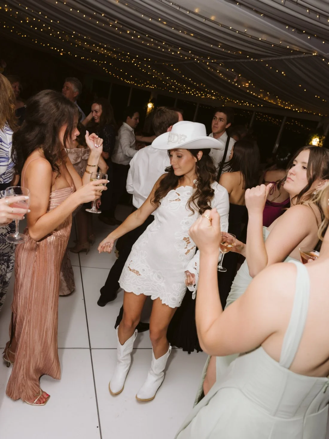 Sydney wearing a white bridal mini dress, cowboy boots, and a white cowboy hat while dancing with Matt at their wedding reception.