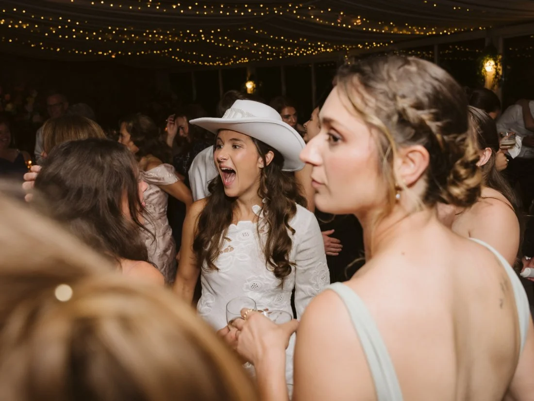 Sydney wearing a white bridal mini dress, cowboy boots, and a white cowboy hat while dancing with Matt at their wedding reception.