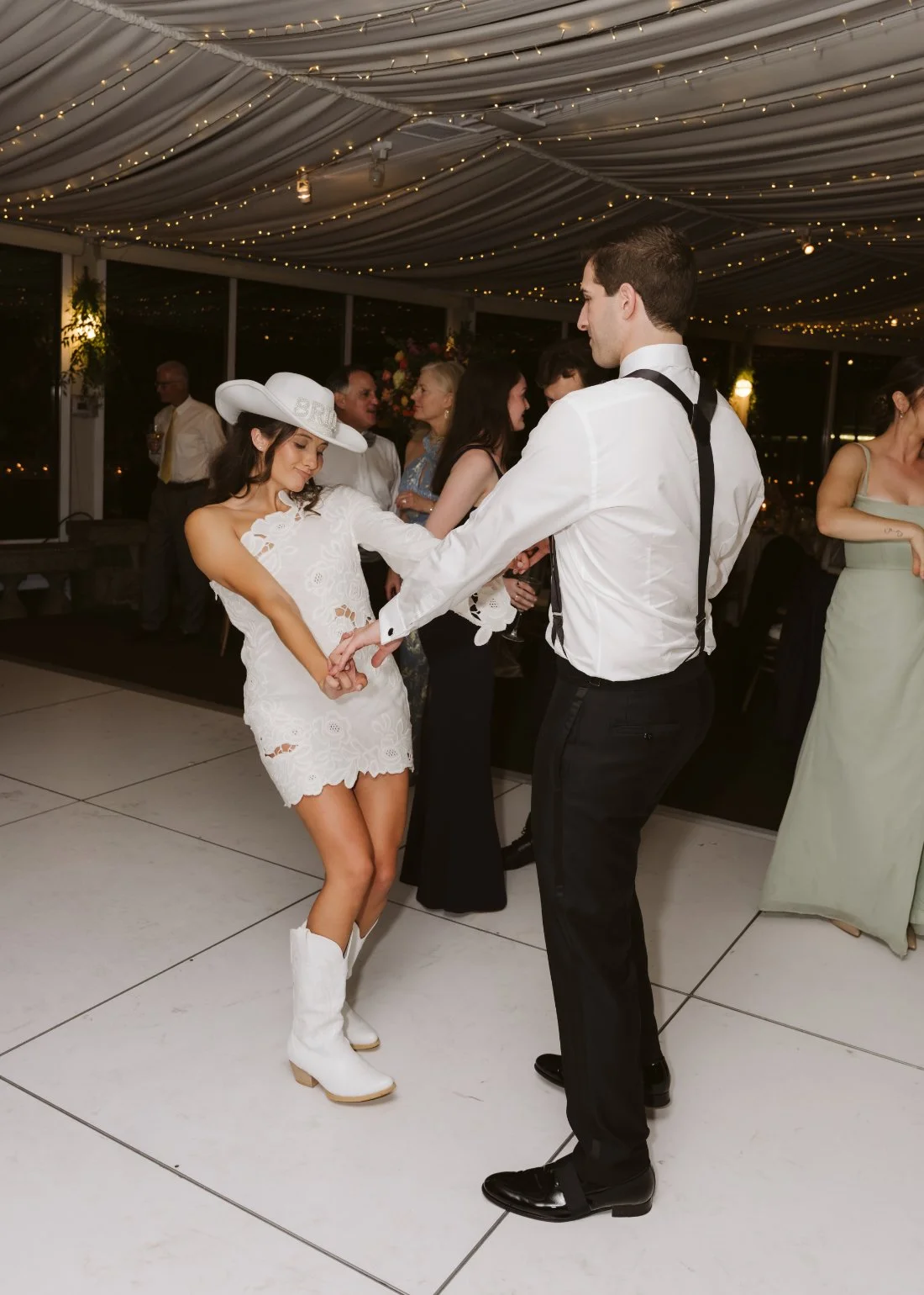 Sydney and Matt celebrating on a packed wedding dance floor with guests beneath twinkling string lights at Tappan Hill Mansion.