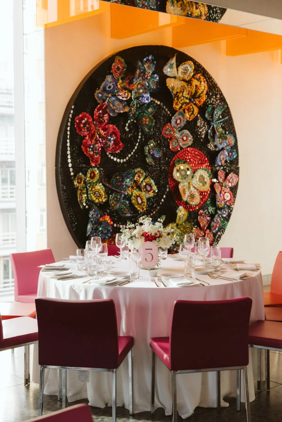 Elegant rehearsal dinner table with pink chairs, white florals, and colorful artwork at Robert restaurant in NYC.