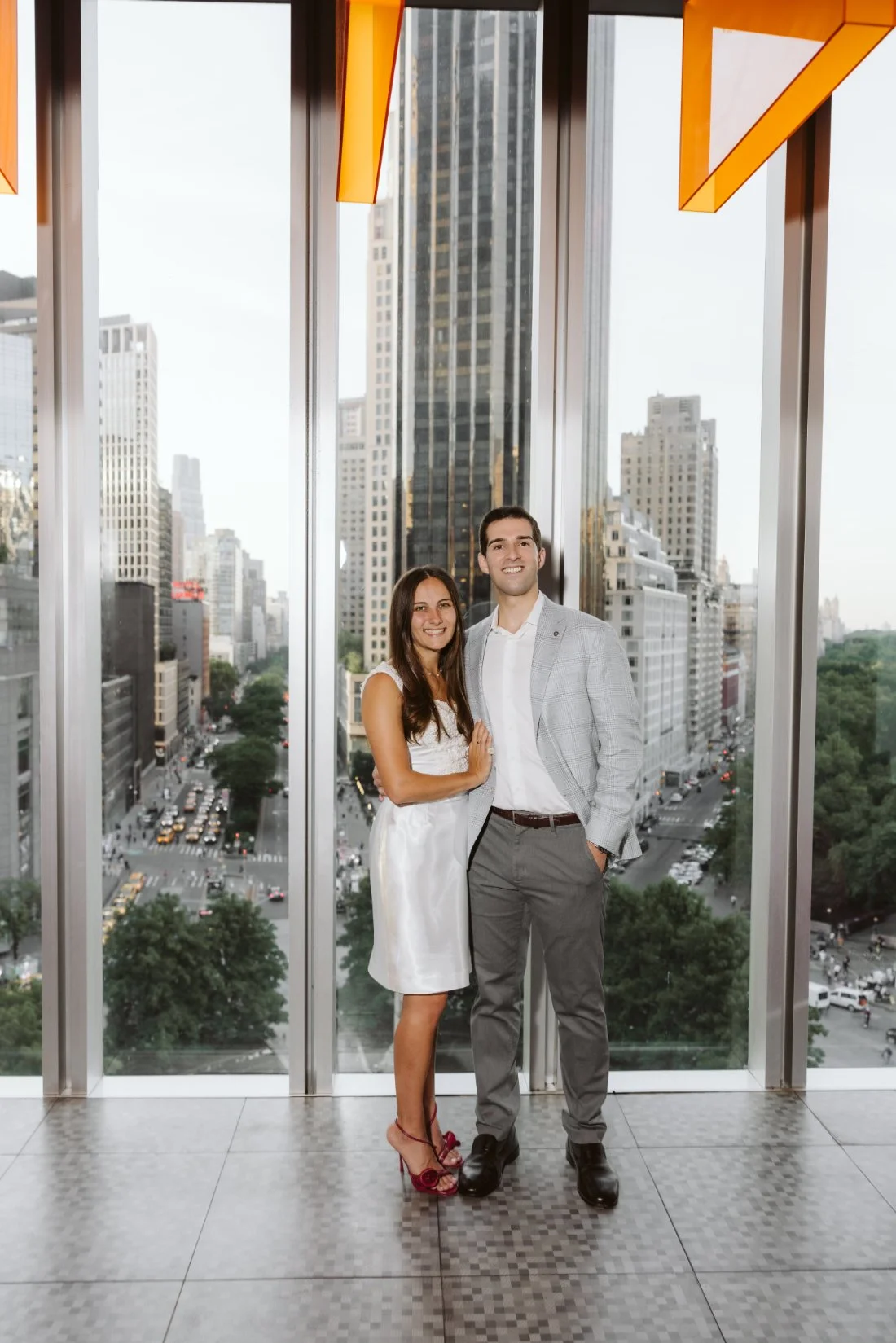 Couple poses together in front of floor-to-ceiling windows overlooking New York City at their rehearsal dinner.