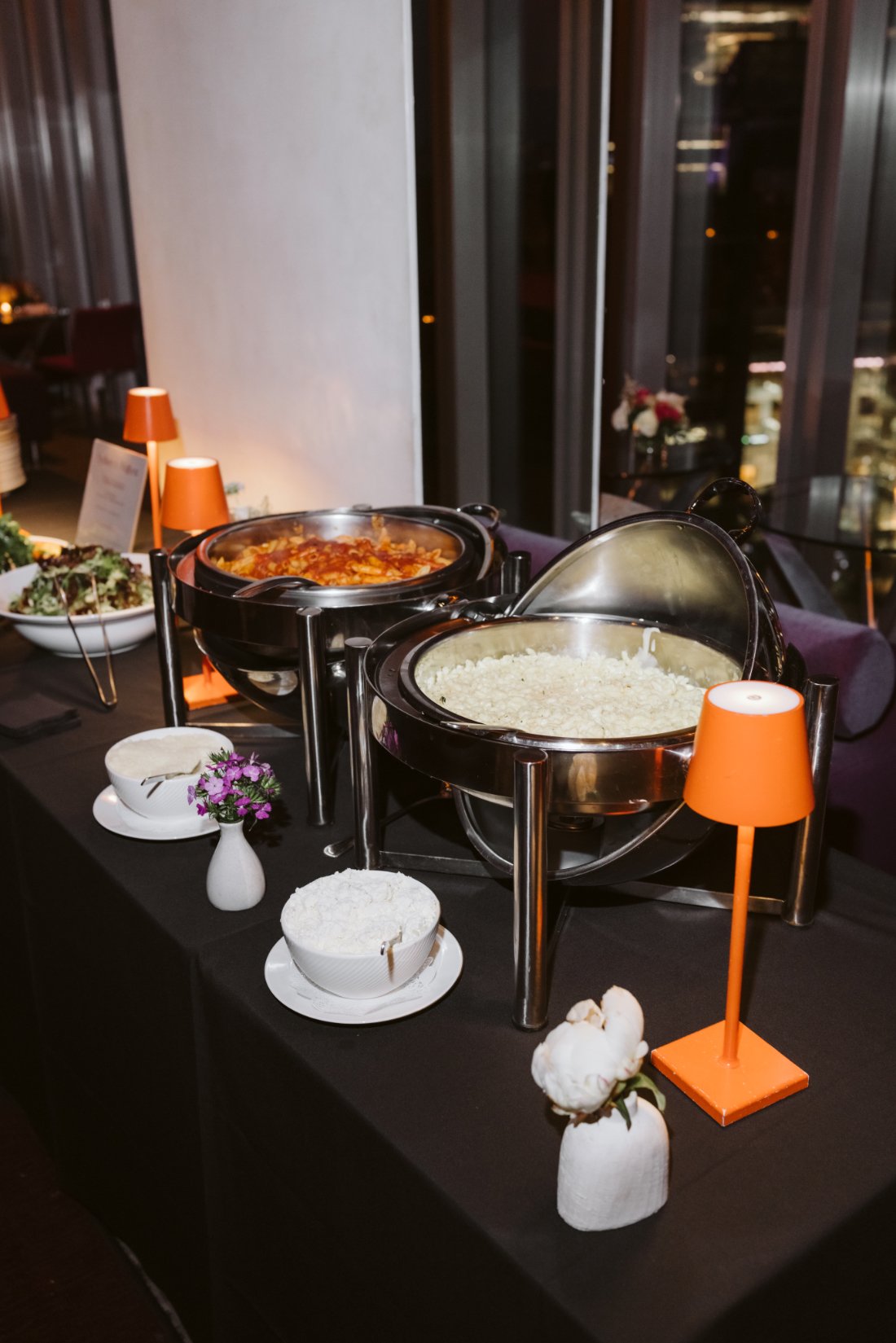 Pink rehearsal dinner pasta station menu displayed between two modern orange table lamps at Robert restaurant.