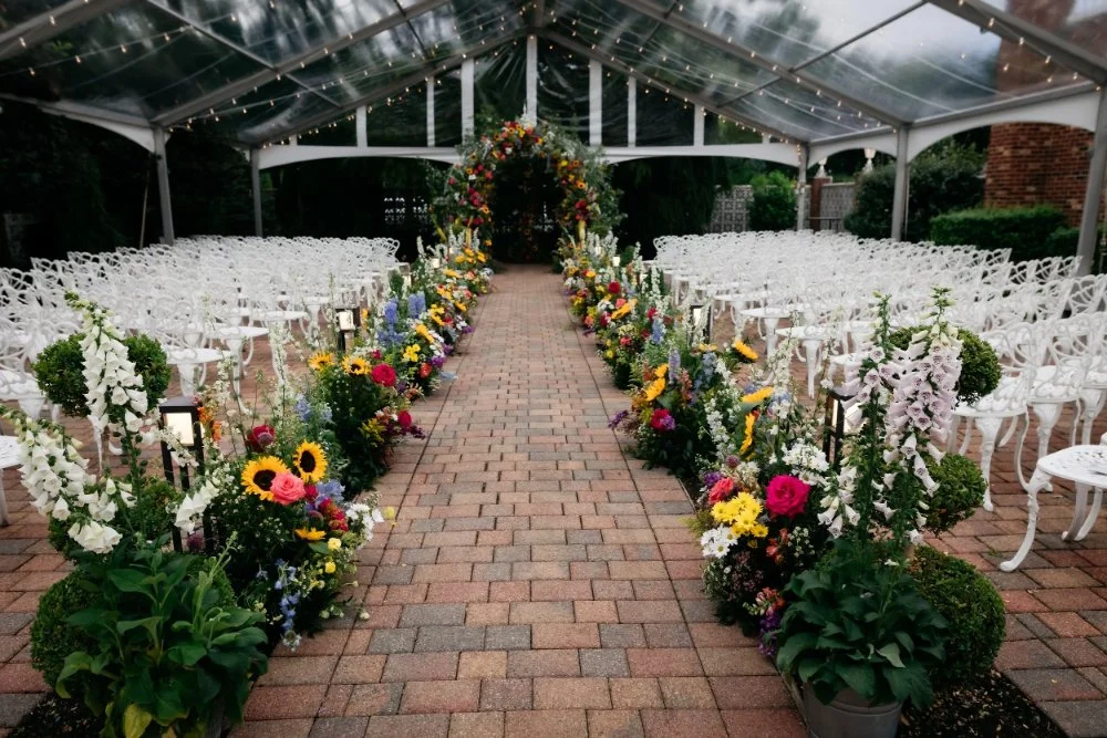 Colorful floral ceremony aisle protected by a clear tent, showing how an outdoor wedding rain plan can preserve the original wedding design