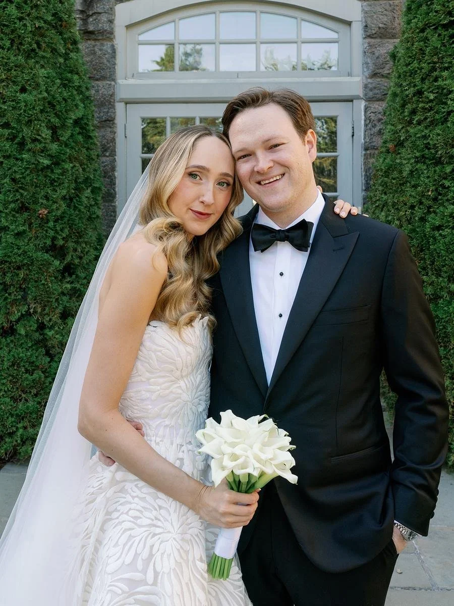Bride and groom pose together outside Wainwright House in Rye, New York, during their elegant fall Wainwright House wedding, with the bride holding a bouquet of white calla lilies and the groom wearing a classic black tuxedo.