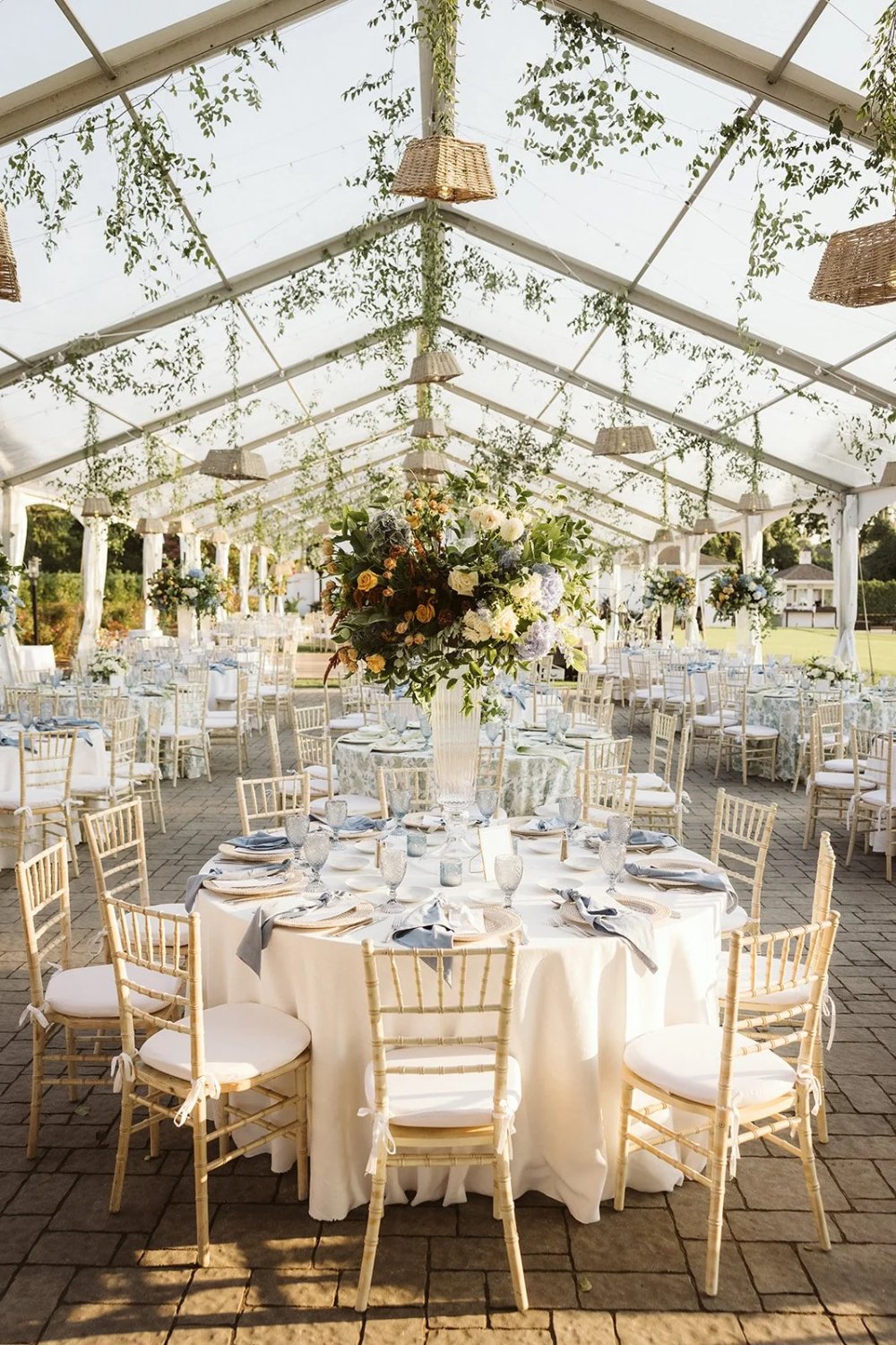 Clear tent with hanging greenery, woven pendant lights, and elegant reception tables as part of an outdoor wedding rain plan