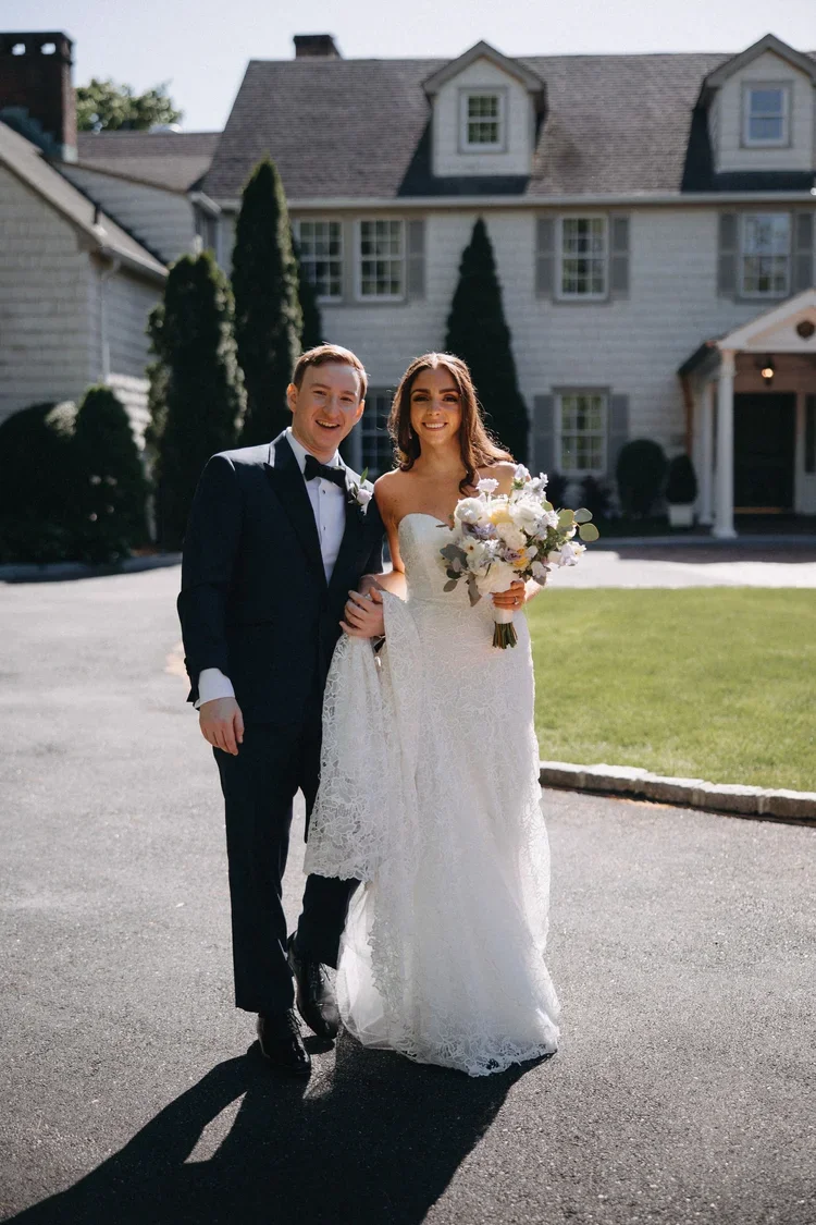 Newlywed couple walking together outside a venue with bouquet in hand, creating a warm and welcoming wedding guest experience
