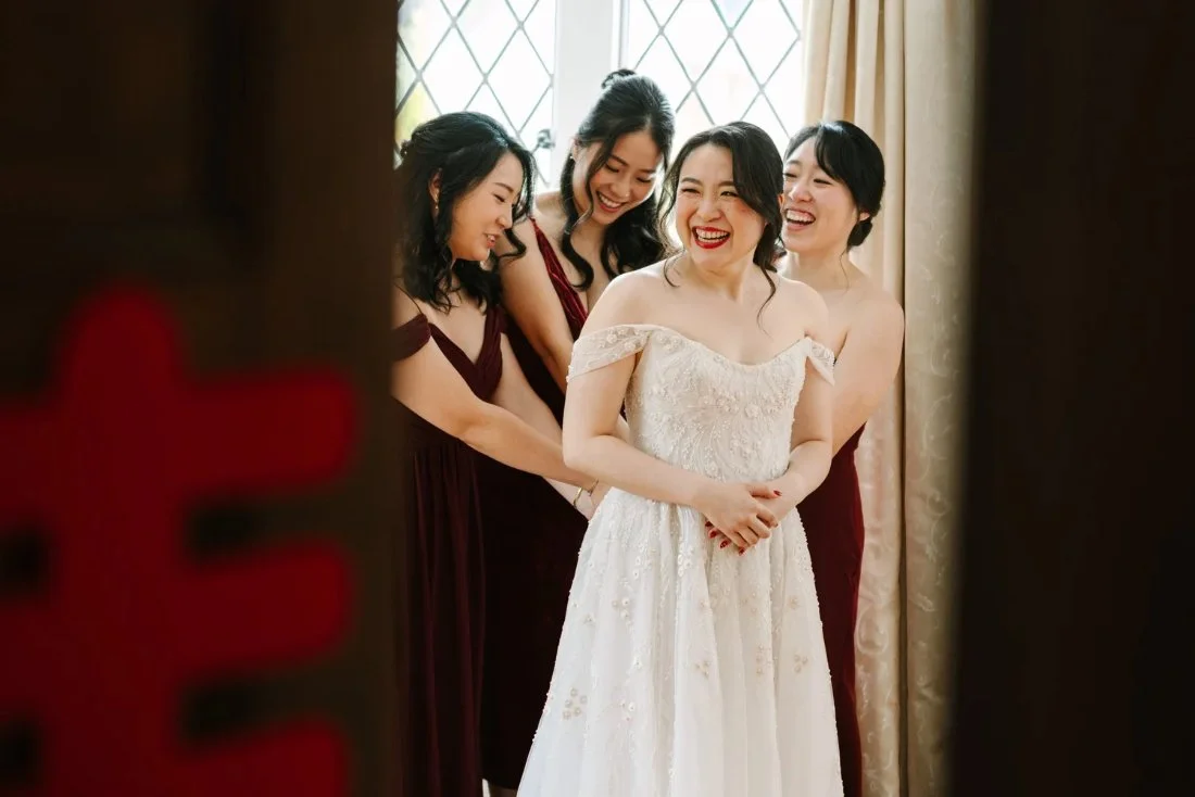 Bride laughing with bridesmaids while getting into her gown, a joyful and candid getting-ready moment