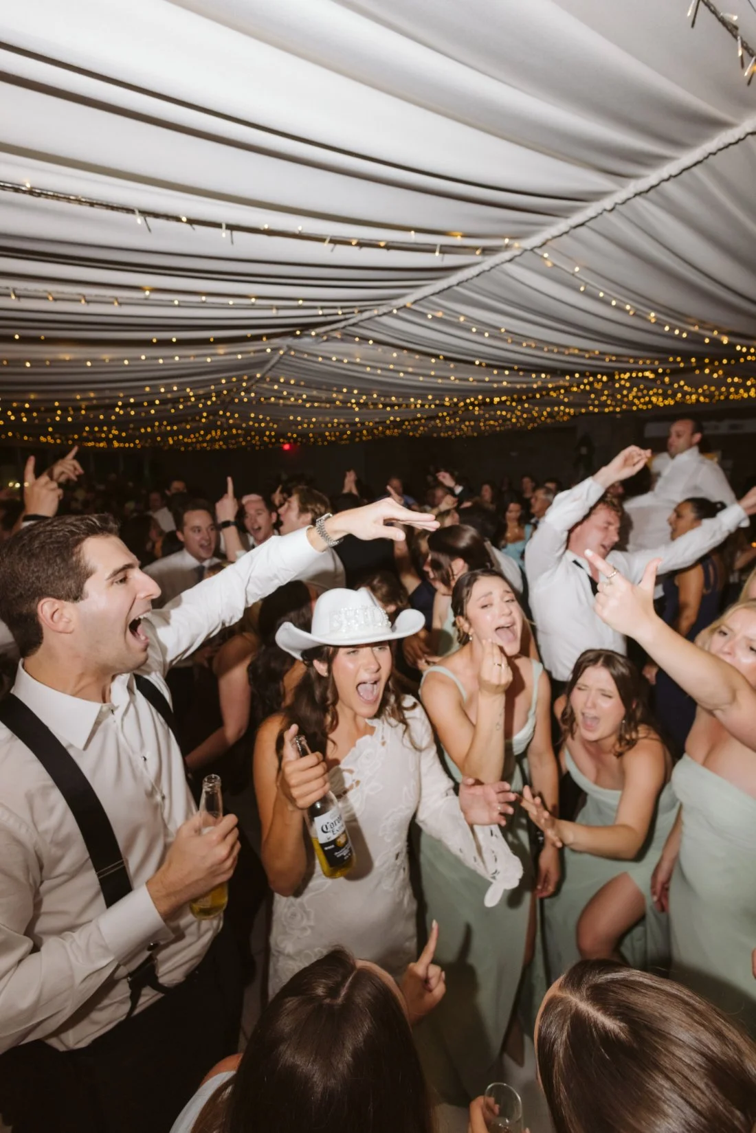 Sydney and Matt celebrating on a packed wedding dance floor with guests beneath twinkling string lights at Tappan Hill Mansion.