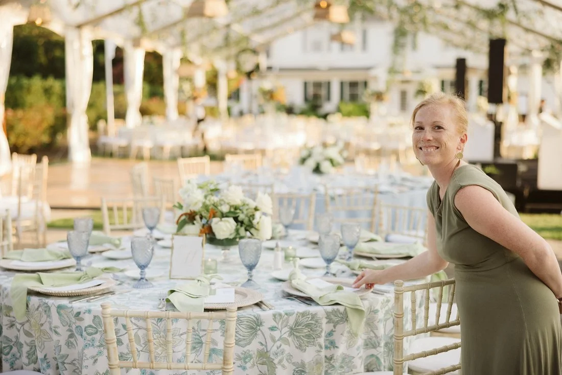 Wedding planner adjusting reception table details under a clear tent, ensuring wedding priorities stay aligned from design to execution.