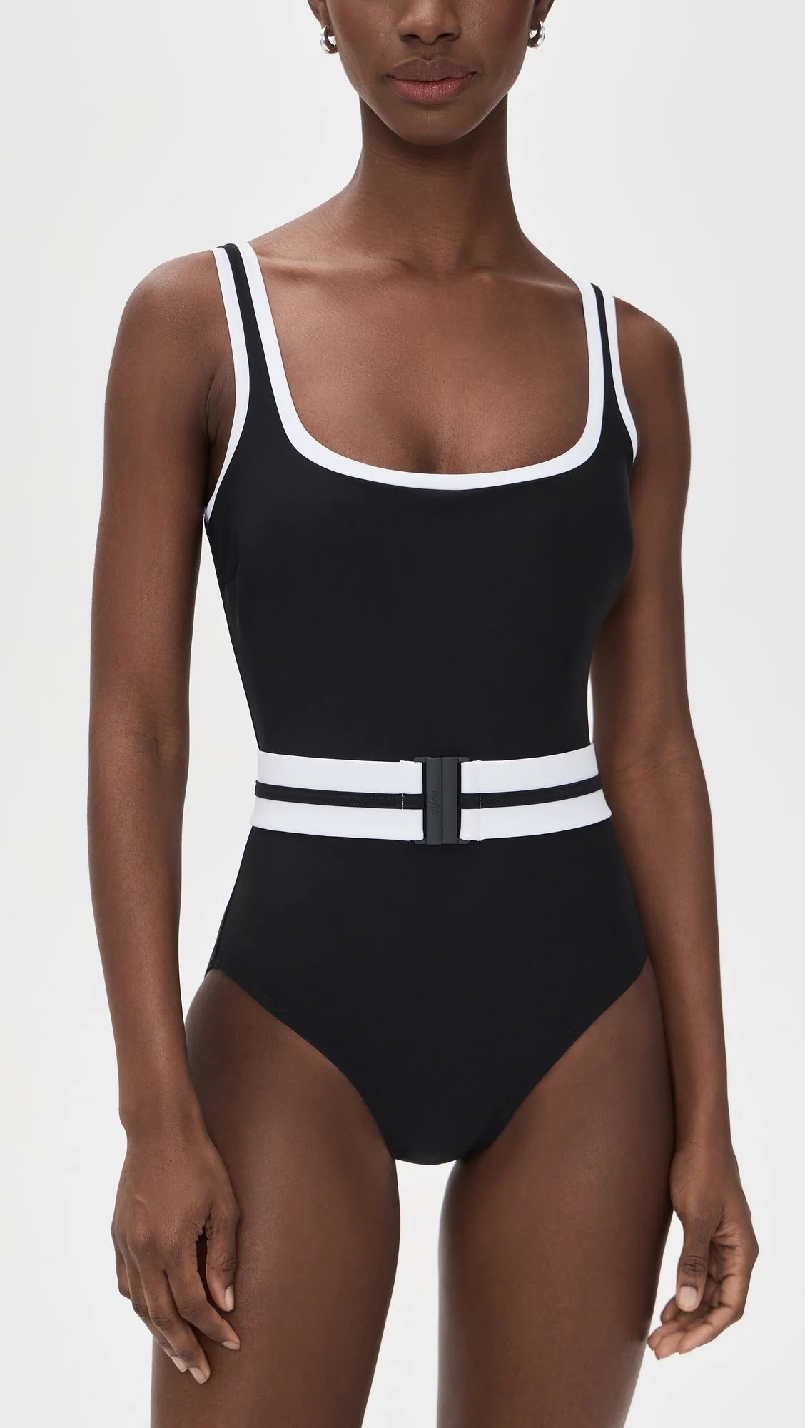 A woman wearing a black sports tank top with white trim and a high-waisted black bottom with a white belt.