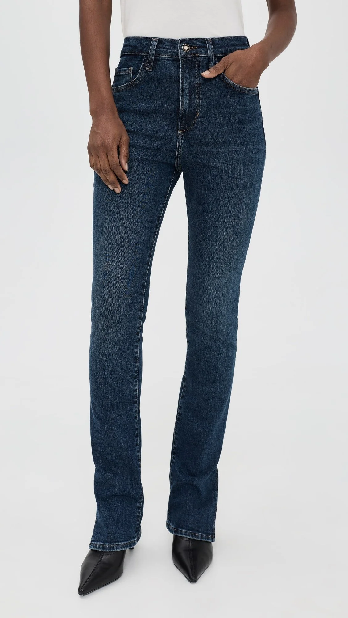 Woman wearing dark blue jeans, tucked into black pointed-toe boots, with one hand in her pocket.