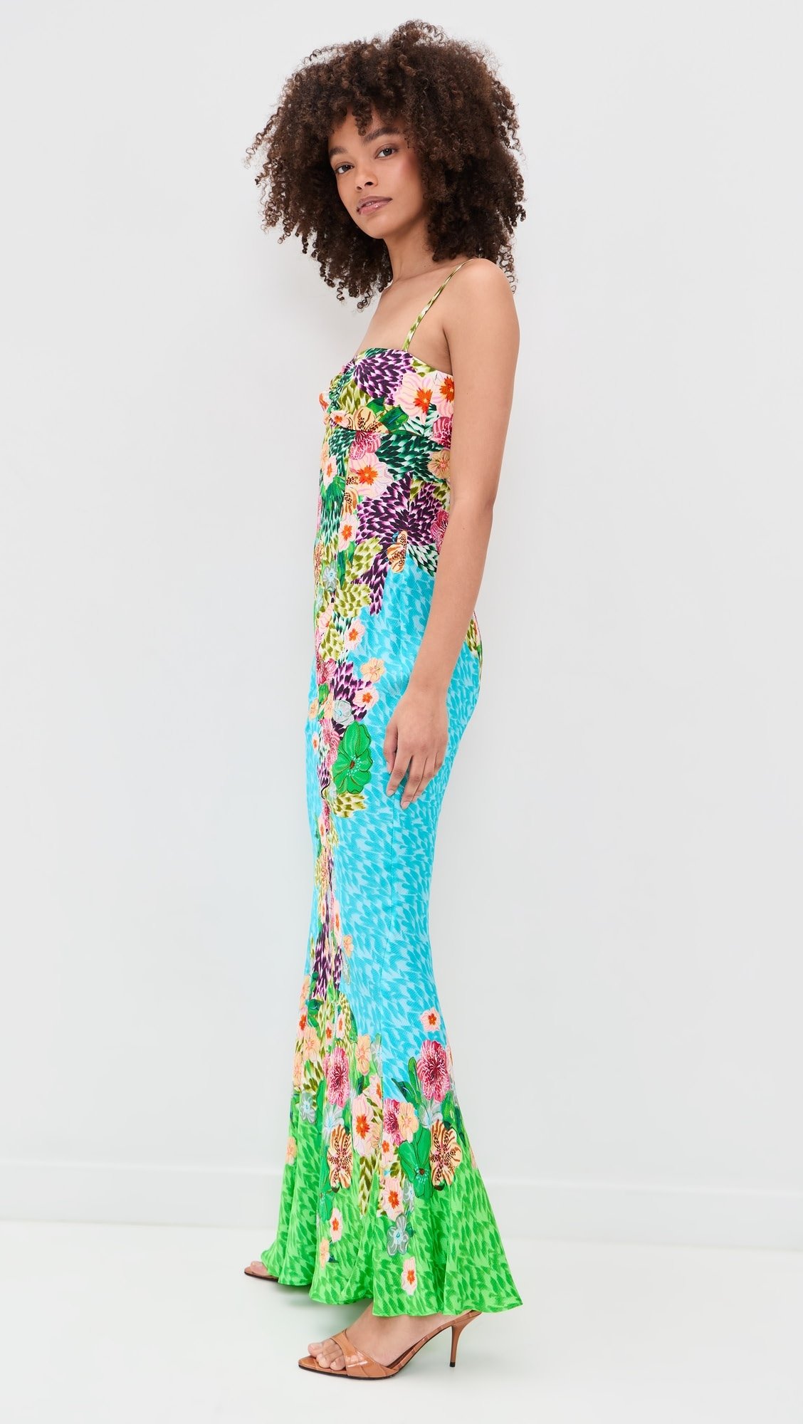 Woman wearing a colorful floral patterned jumpsuit with a fitted top and flared pants, standing against a plain white background.