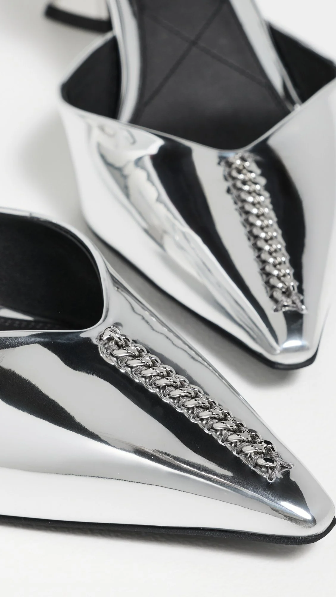 Close-up of a shiny black and silver high heel shoe with a silver chain embellishment along the back.