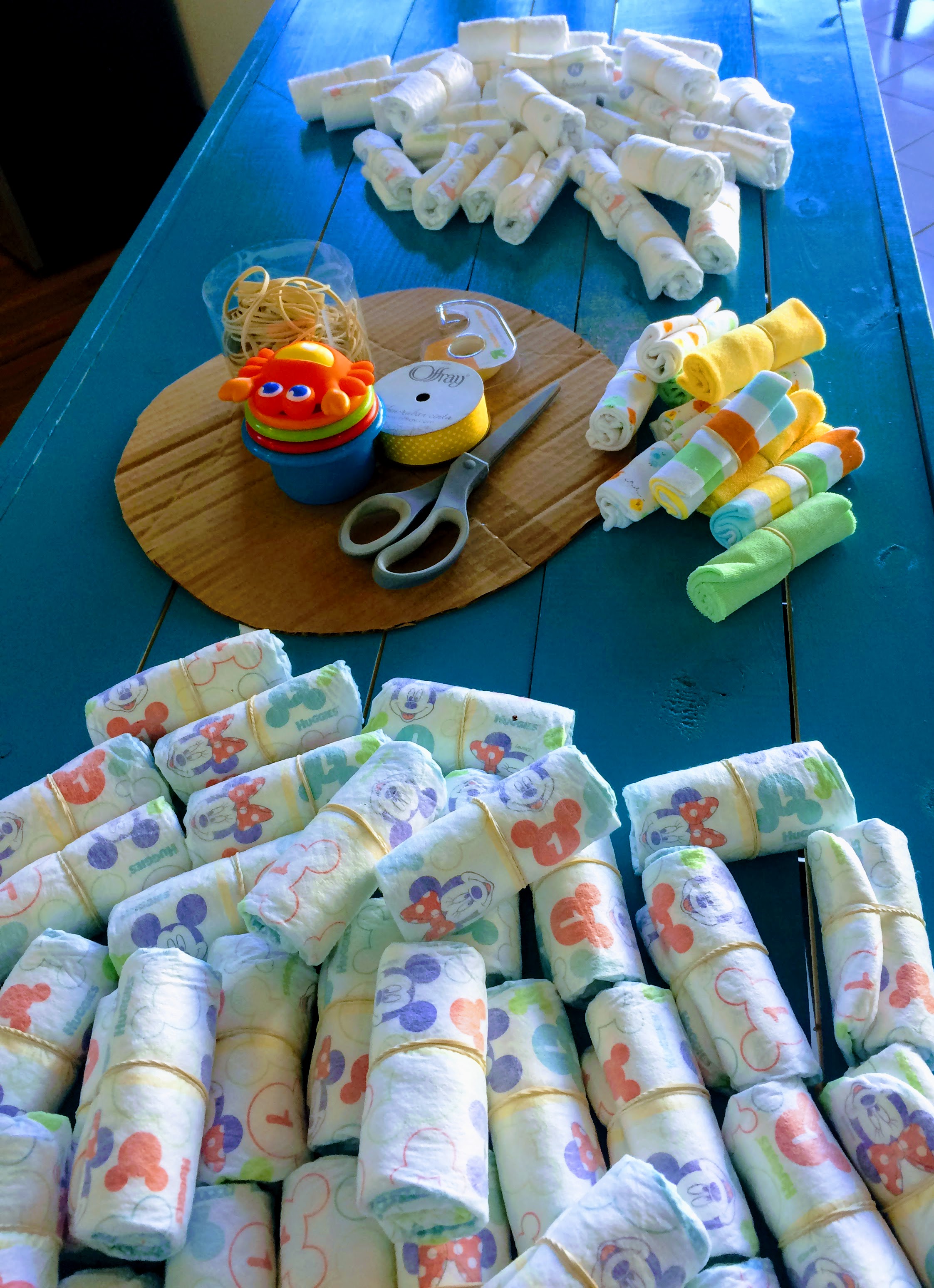 Now you're ready to get started! Roll all of your diapers (and other 'cake' materials) up, starting with the open end of the diaper. Secure each around the middle with a rubber band. It helps if you place the rubber band in close to the same spot on each diaper, so you can easily cover them up with ribbon later. Some diapers have a yellow line down the middle as a wetness indicator, and this can be very useful when attempting to position the band in the same spot.