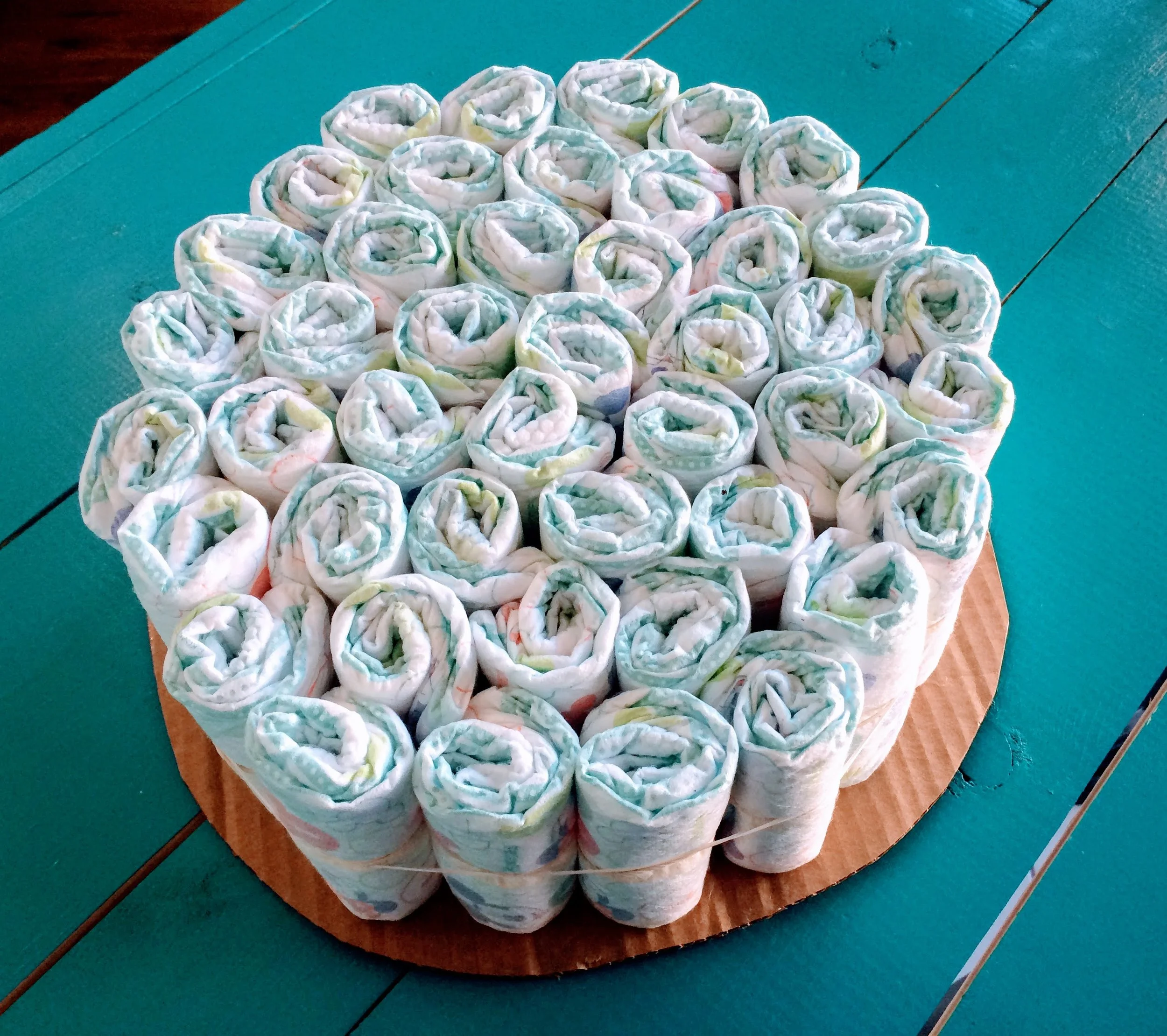 Next, gather all of your biggest diaper size together to form the bottom cake layer. You'll need a large rubber band for this part. If you have a helper, have them hold as many as possible while you set the rubber band around them. If you're doing it solo, just put as many as you can inside the rubber band to start, and continue adding around the outside, Rubber bands are stretchy - don't worry!