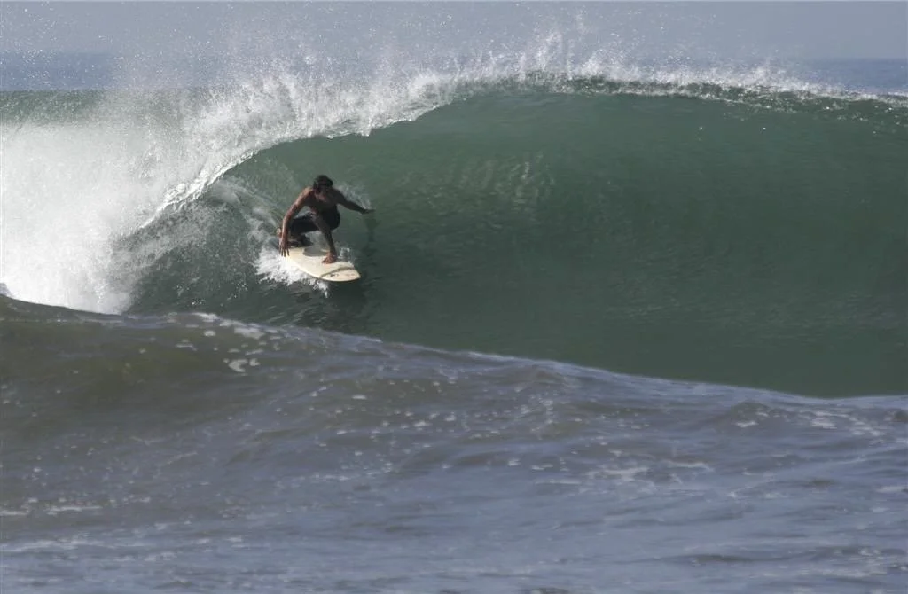 A person surfing on a large wave in the ocean almost completely in the tube.