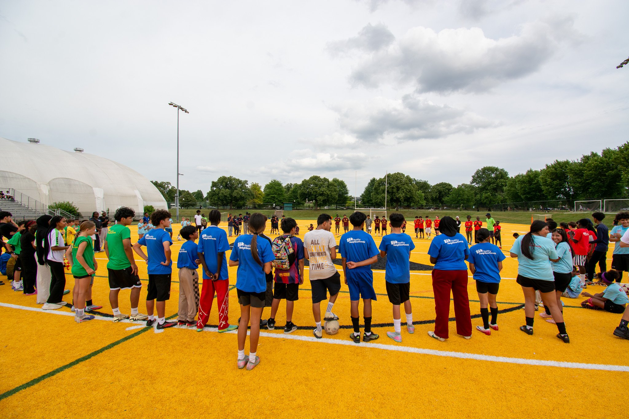  Elementary and Middle School youth from across Southeast Baltimore kicked off the World Cup-themed soccer tournament meeting in a circle on Utz field in their new country-themed T-shirts 