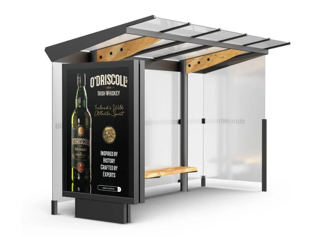 A modern bus shelter with an advertisement for O'Driscoll Irish Whiskey on the side panel, featuring a large bottle of whiskey, and a wooden bench inside.