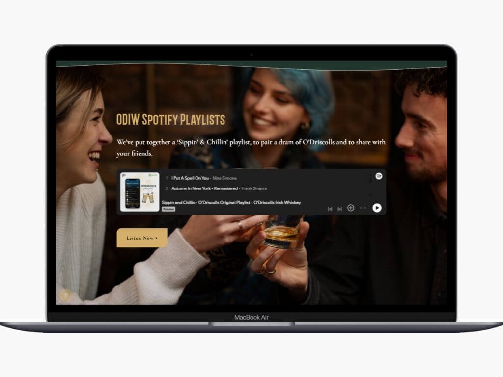A MacBook Air displaying a Spotify playlist titled 'ODIW Spotify Playlists' with a picture of three friends laughing and sharing drinks, and a yellow button labeled 'Listen Now'.