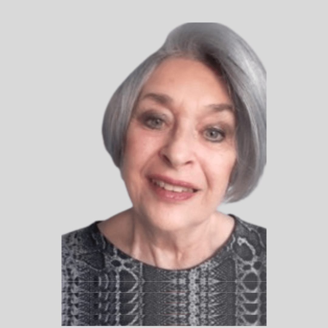 A middle-aged woman with short gray hair, light skin, and blue eyes, smiling and wearing a black and gray patterned top, against a plain light gray background.