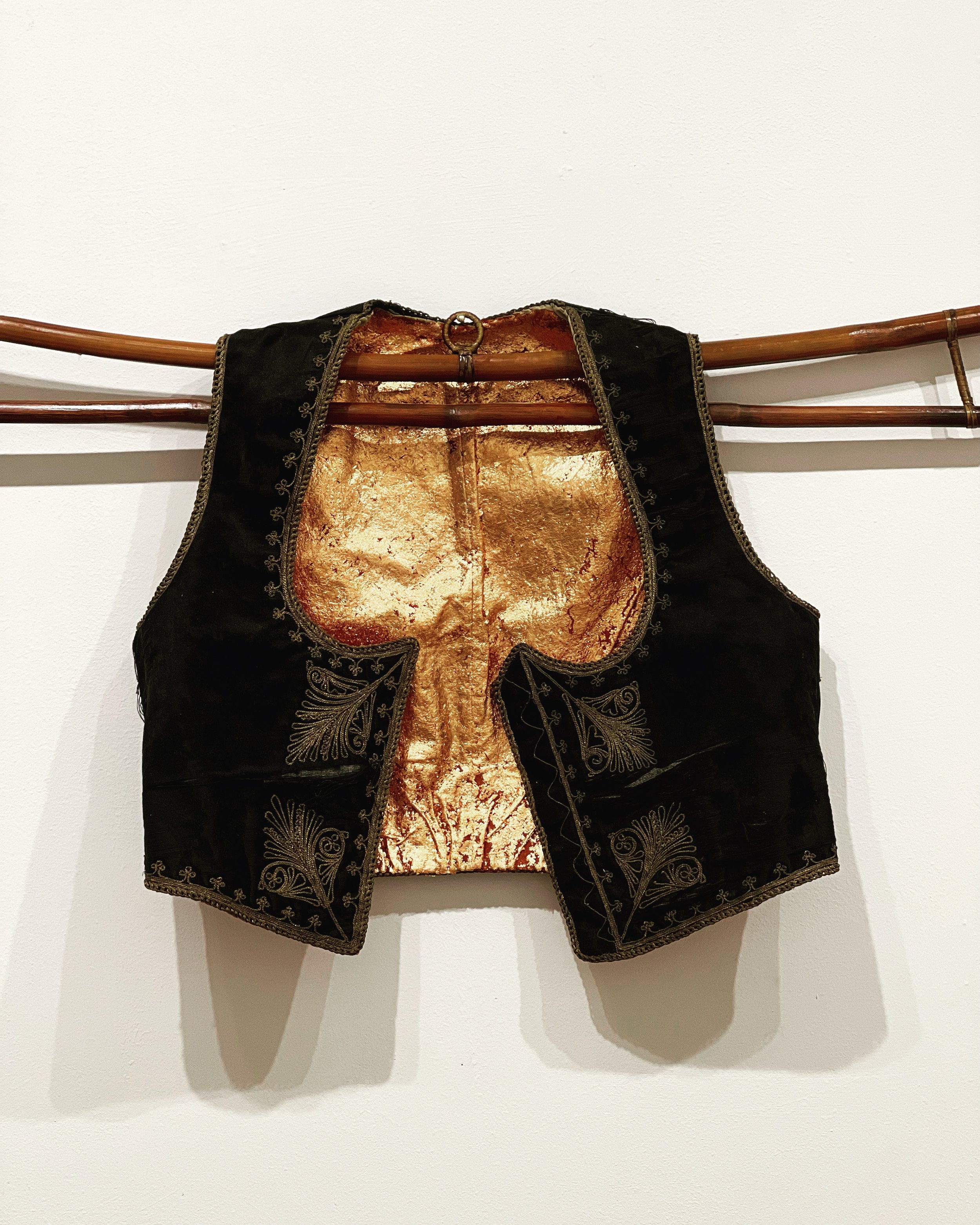   Vested Interest , 2022  Velvet, silk, cotton, copper gilding  15 x 16 inches   $610.   An antique woman’s velvet and silk vest covered with copper gilding and displayed on a bamboo hanger.  