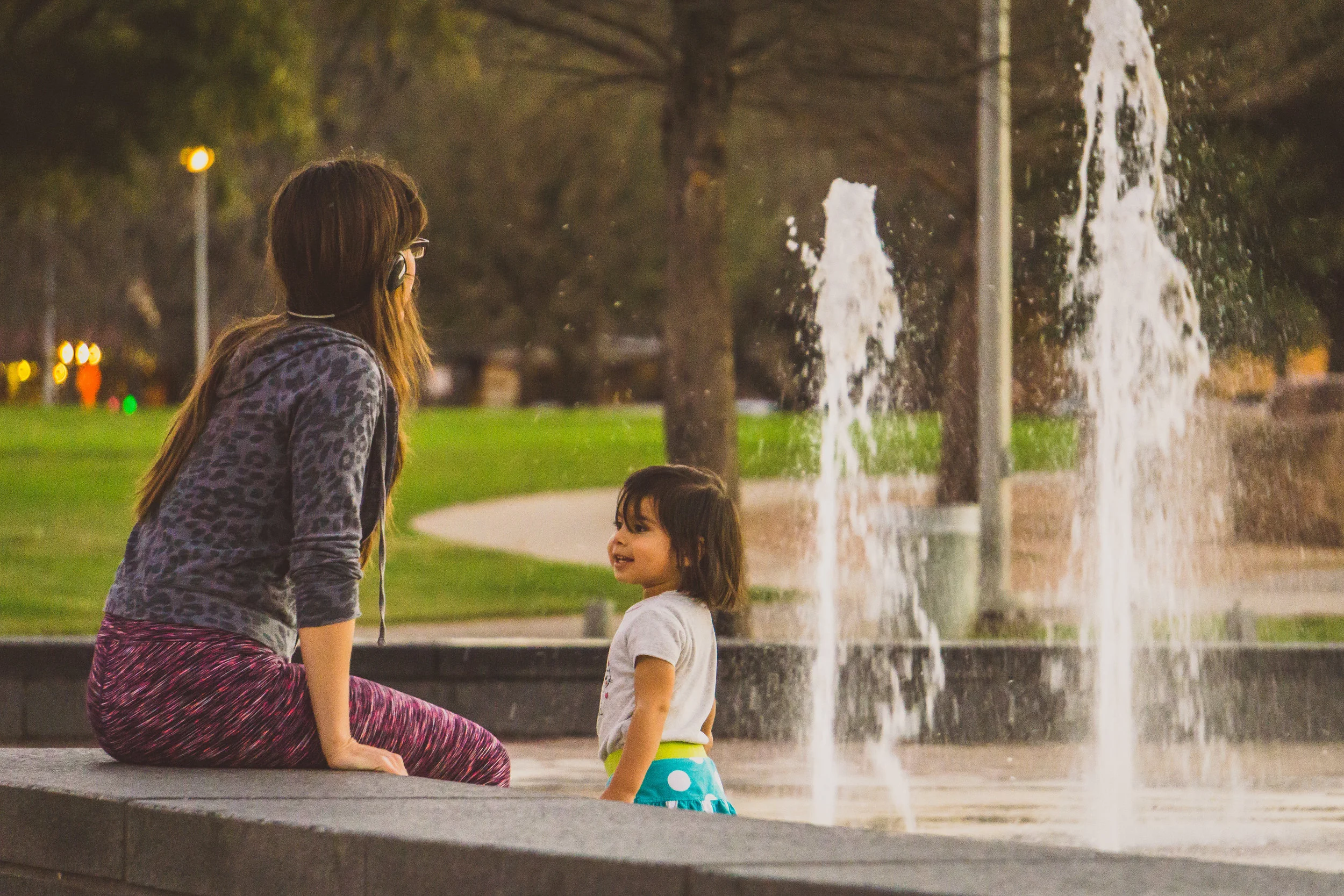 A mother and daughter enjoy the warm winter twilight in the Liz Carpenter Splash Pad fountains.