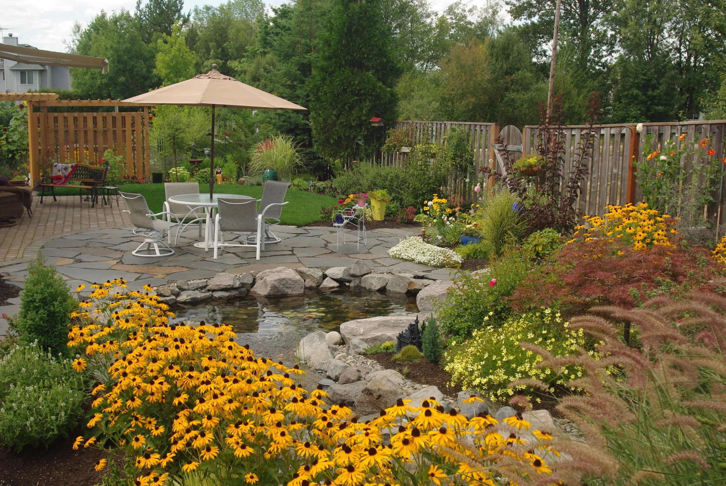 Relaxing pond, yellow hued blooms, flagstone and pavers all come together