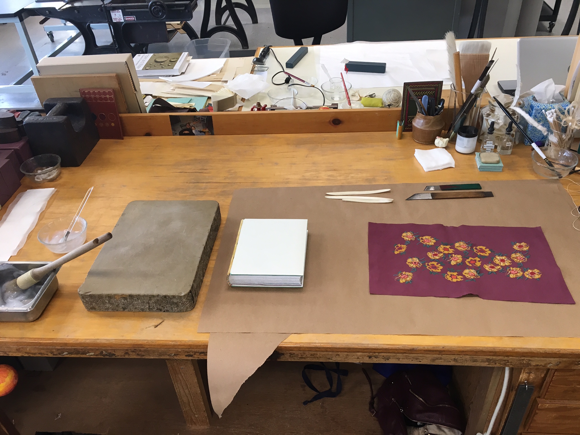 My bench set up before covering. You can see my paste, a litho stone, the binding (which I still had to cap up!), a few bone folders useful for forming headcaps and corners, paring knives, and the covering skin. 