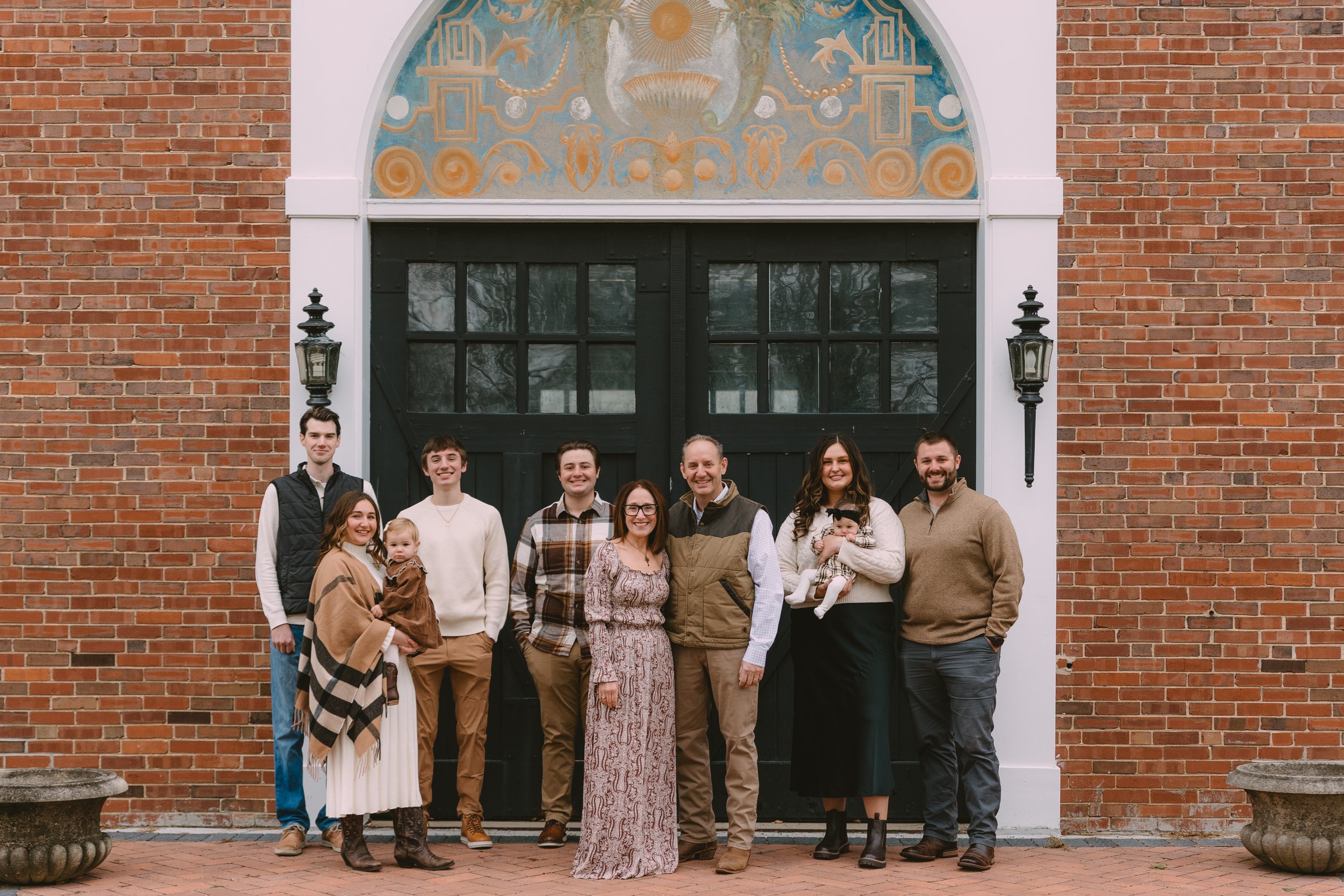 A family group of ten people, including two young children, standing in front of a large black-gate door with a decorative arch and brick wall. It appears to be a family photo outdoors.

Kaitlyn Johnston Photography | Chicago Portrait Photographer