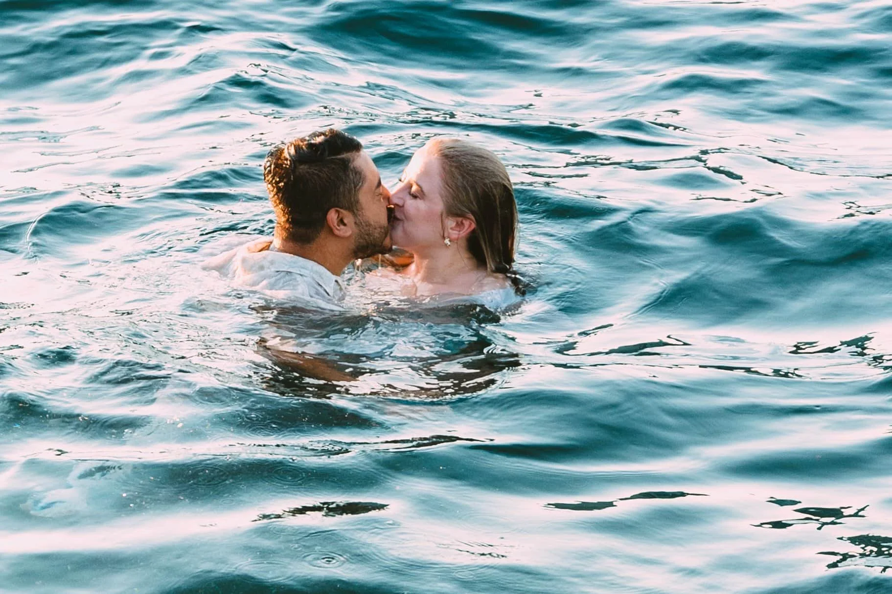 A couple is kissing in Lake Michigan during sunset, with gentle ripples on the water surface.