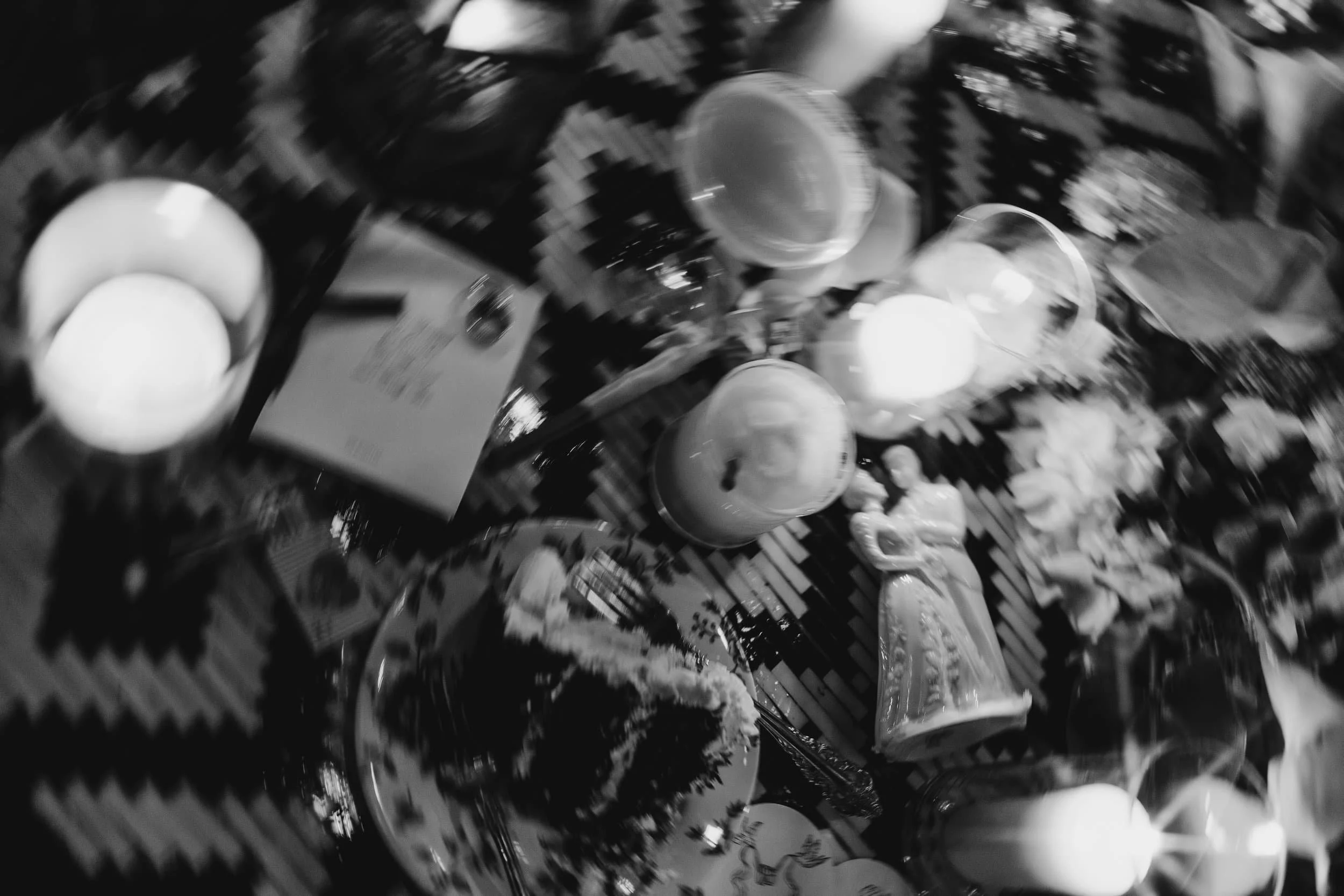 A table with various food items and beverages, including eggs in a bowl, a bottle, a figure of a woman, and other dishes, with a patterned tablecloth.