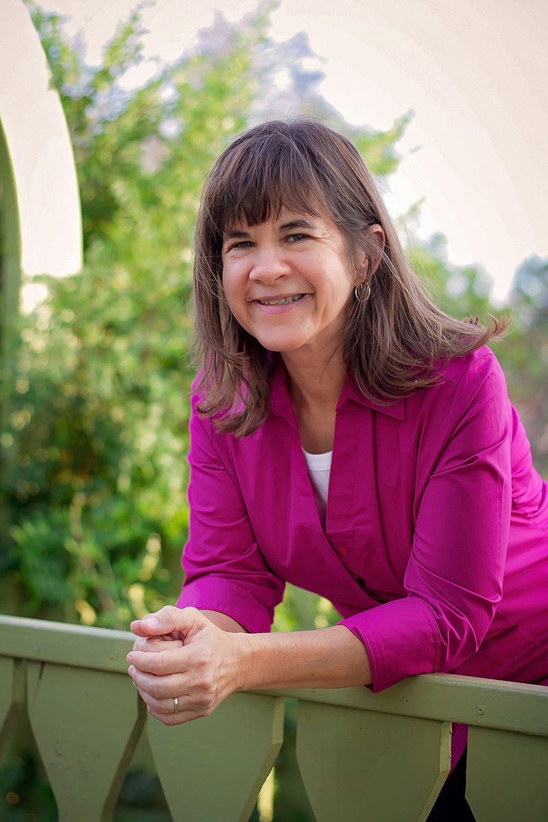 Woman in a pink shirt leaning over green fence.jpg