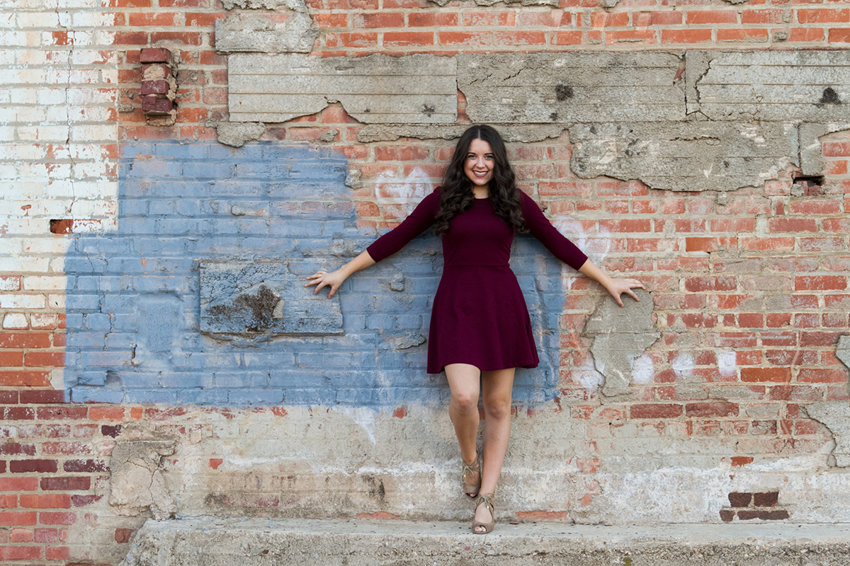 Senior Girl in Red Dress holding onto brick wall.jpg