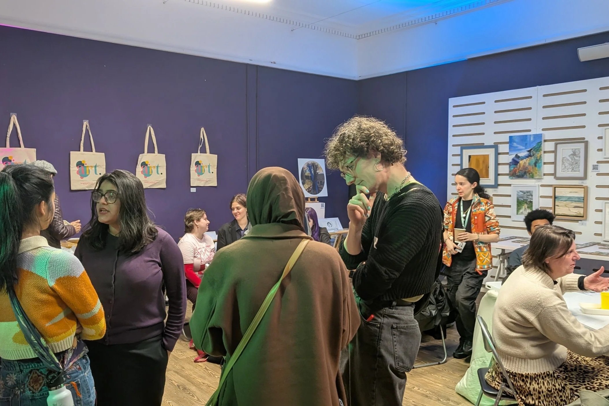 A group of people chatting at an event in an art gallery with dark purple walls
