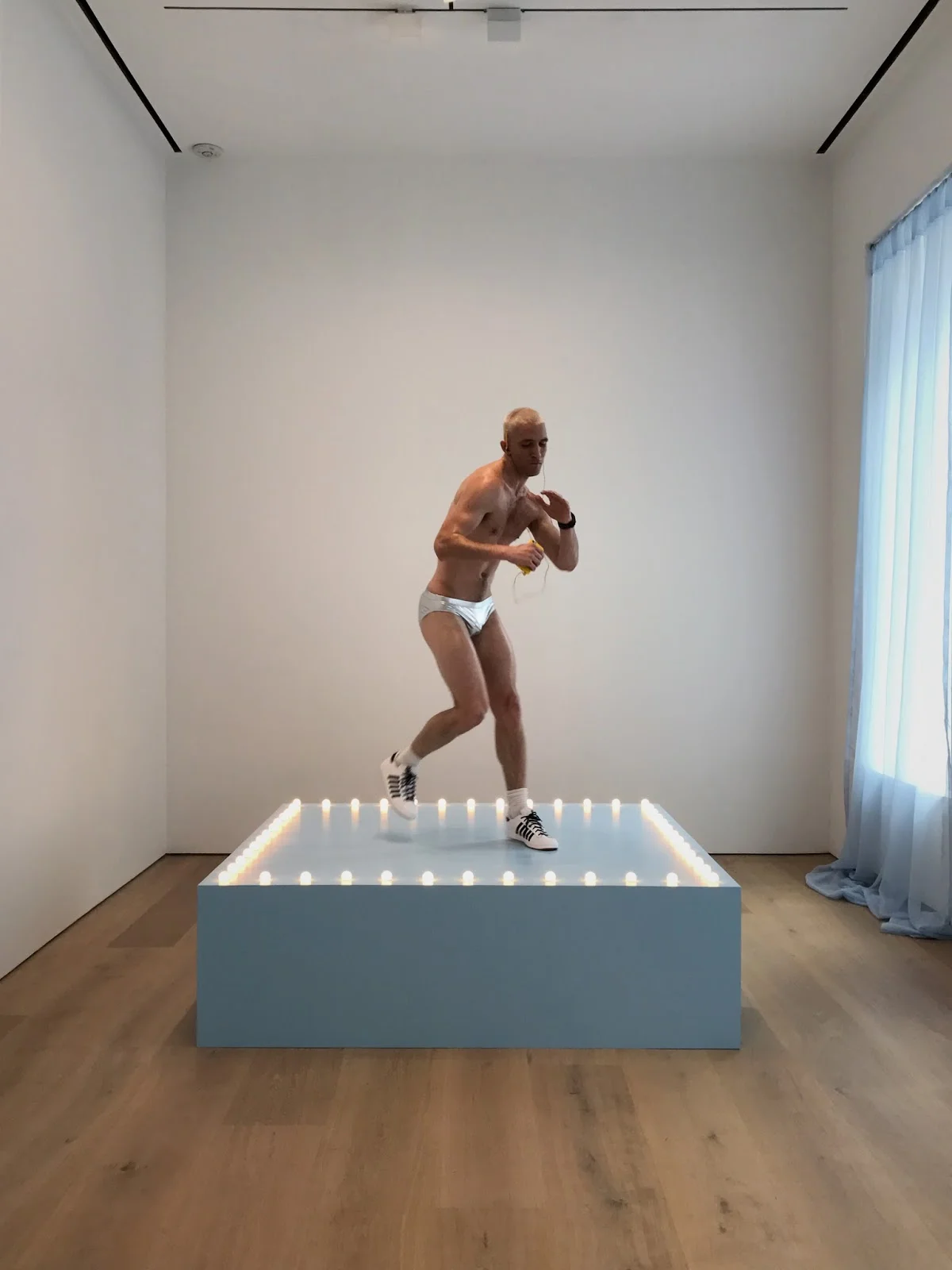 Felix Gonzalez-Torres, “Untitled” (Go-Go Dancing Platform) (1991), wood, light bulbs, acrylic paint, and Go-Go dancer in silver lamé bikini, sneakers, and personal listening device; overall dimensions vary with installation; platform: 21 1/2 x 72 x 72 in