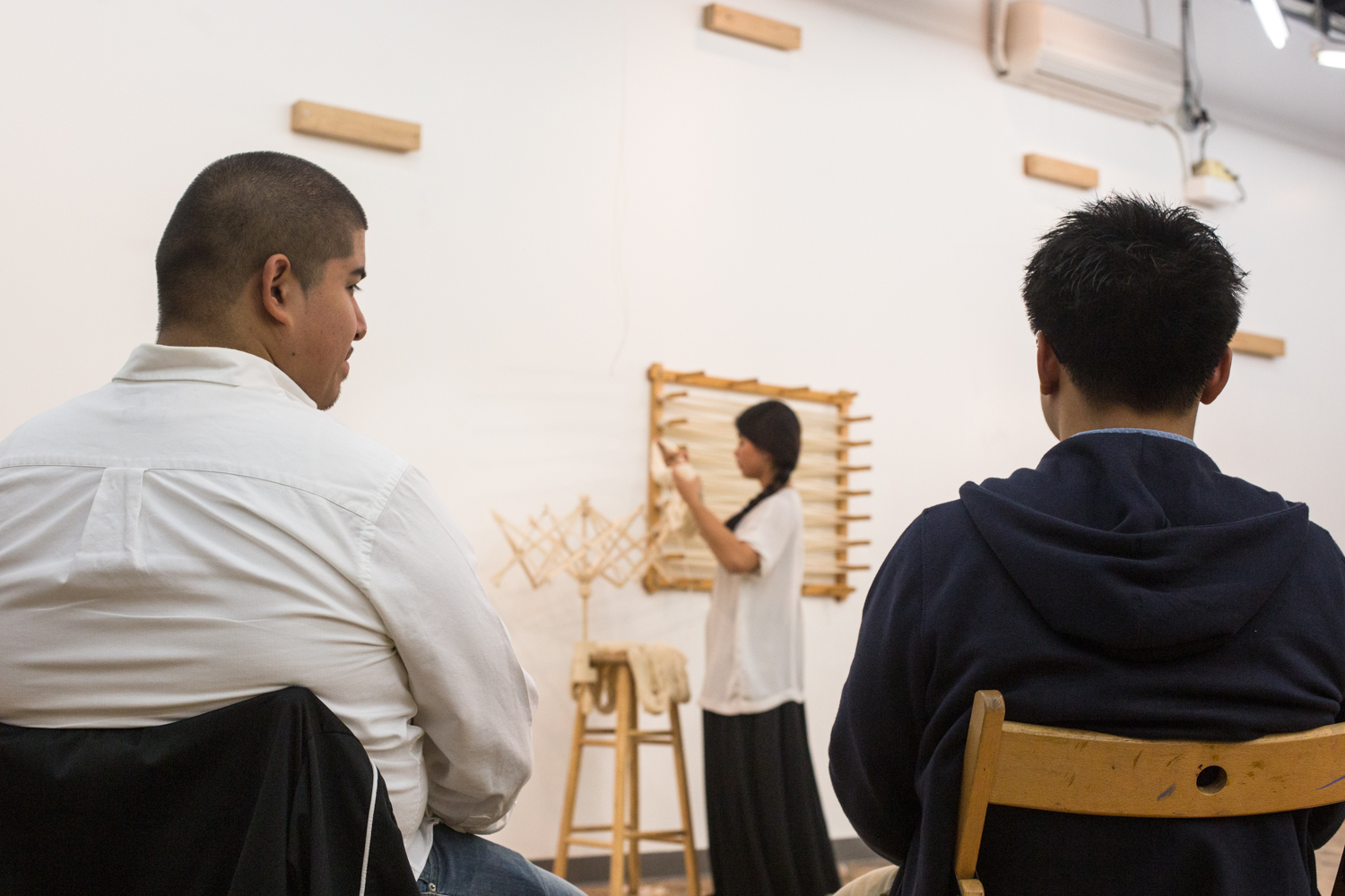 Two audience members watching the performance with the artist blurred in the background. She is counting the number of times the yarn is wrap around her hand as a representation of days.