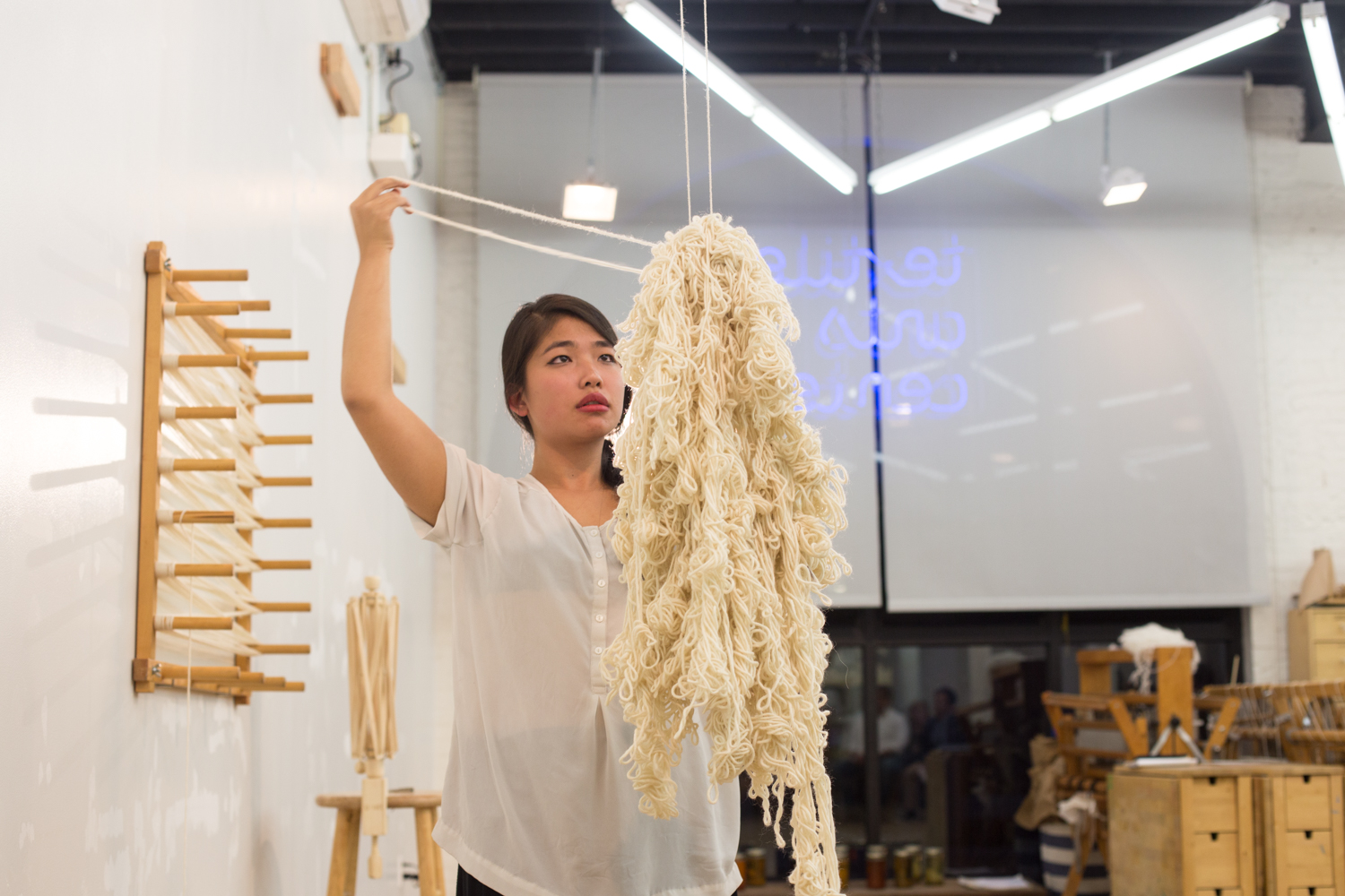 The heap of knotted yarn is picked up from the floor and suspended in the air by a string hung from the ceiling. The artist begins to unknot and unravel the yarn that she has knotted previously.