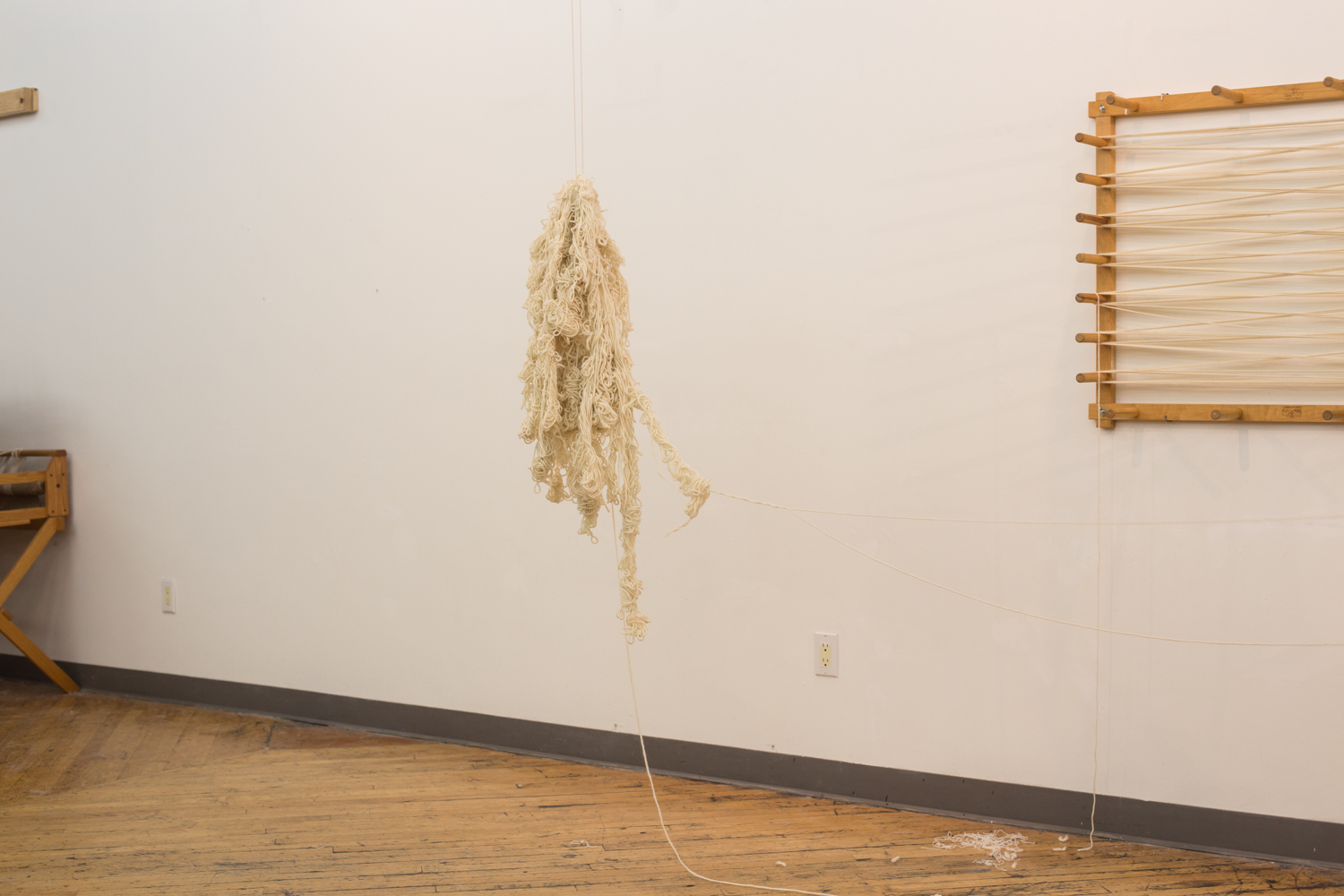 The knotted yarn is suspended with the warping board in the background. The artist is not visible.