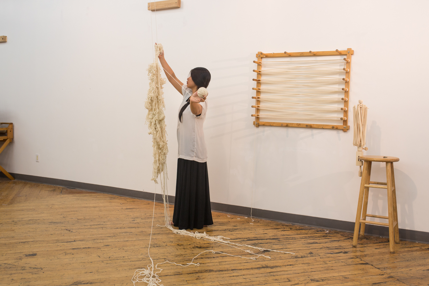 The artist holds a ball of yarn (around 1 inch in diameter) that she has untangled in her left hand as she continues to unravel with her right hand. Three-fourth of the knotted yarn has been unraveled.